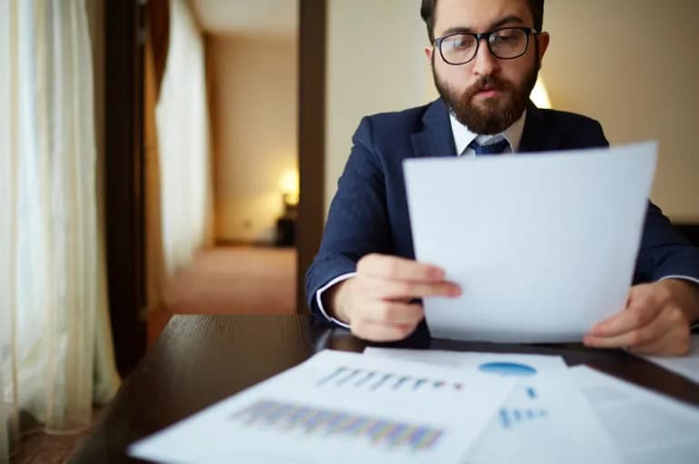 Homem de terno sentado em uma mesa analisando papel